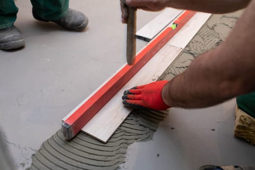 Spirit level - a device for checking the correctness of works performed in relation to the level. A professional construction worker. Kneeling.