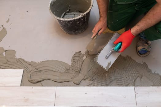 Professional construction worker laying ceramic tiles on the floor in the bathroom room.