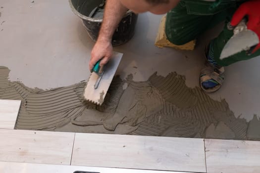 Professional construction worker laying ceramic tiles on the floor in the bathroom room.