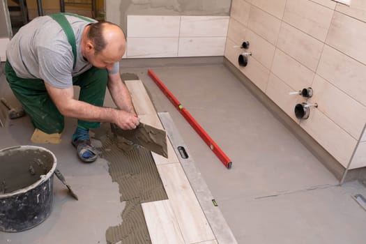 General construction worker. Adhesive for ceramic tiles. The builder glues terracotta to the floor.