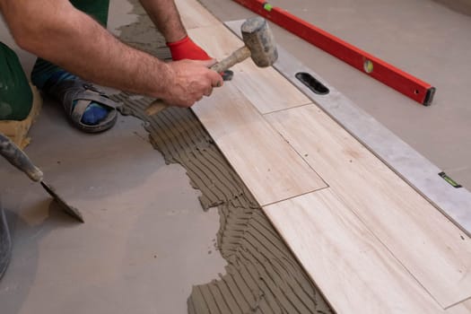 Rubber hammer. An experienced construction worker. Laying terracotta in the bathroom. Work clothes. He knocks with a hammer.