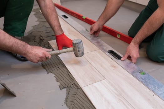 Rubber hammer. An experienced construction worker. Laying terracotta in the bathroom. Work clothes. He knocks with a hammer.