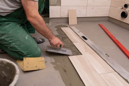 Professional construction worker laying ceramic tiles on the floor in the bathroom room.