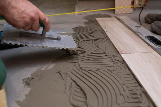 Professional construction worker laying ceramic tiles on the floor in the bathroom room.