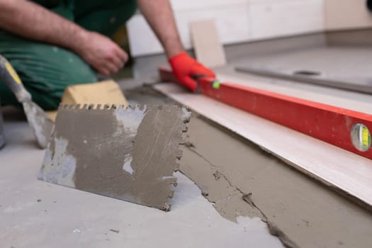 Spirit level - a device for checking the correctness of works performed in relation to the level. A professional construction worker. Kneeling.
