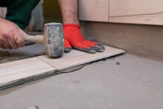Rubber hammer. An experienced construction worker. Laying terracotta in the bathroom. Work clothes. He knocks with a hammer.
