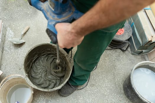 Electric stirrer. Mixing cement based adhesive. A professional construction worker. A bucket full of crushed adhesive for ceramic tiles.