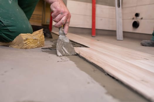 Professional construction worker laying ceramic tiles on the floor in the bathroom room.