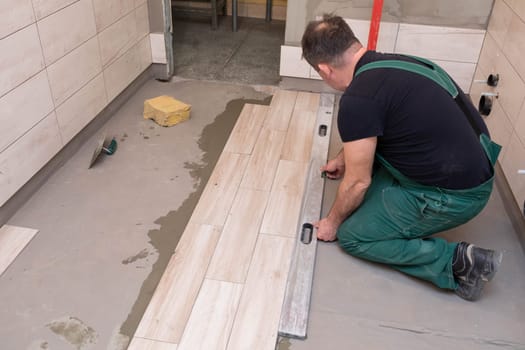Spirit level - a device for checking the correctness of works performed in relation to the level. A professional construction worker. Kneeling.