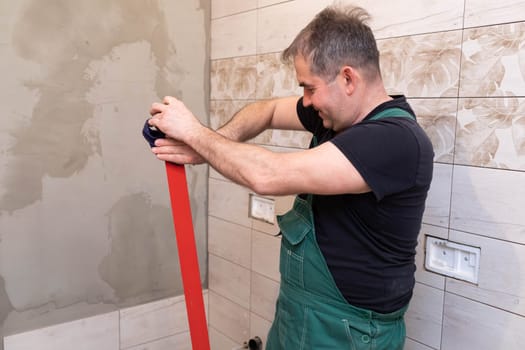 Red spirit level. Washes measuring tools with a wet cloth. Middle-aged manual worker. General construction worker.