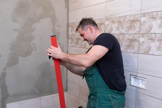 Red spirit level. Washes measuring tools with a wet cloth. Middle-aged manual worker. General construction worker.