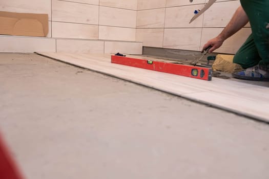 Professional construction worker laying ceramic tiles on the floor in the bathroom room.