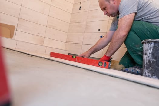 Professional construction worker laying ceramic tiles on the floor in the bathroom room.