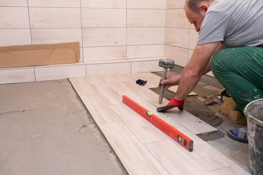 Professional construction worker laying ceramic tiles on the floor in the bathroom room.