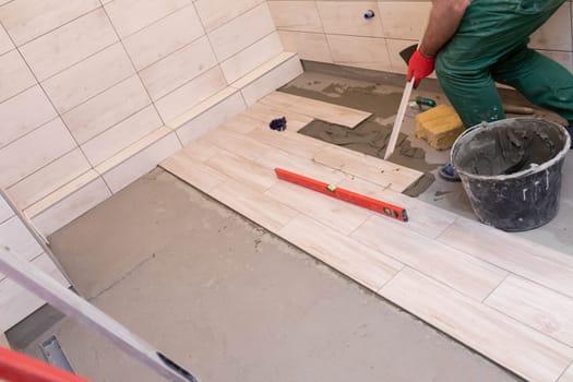 Professional construction worker laying ceramic tiles on the floor in the bathroom room.