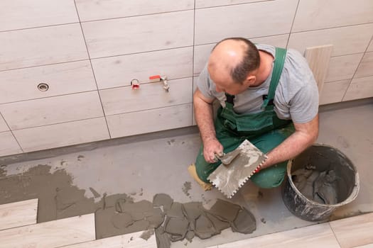 Professional construction worker laying ceramic tiles on the floor in the bathroom room.