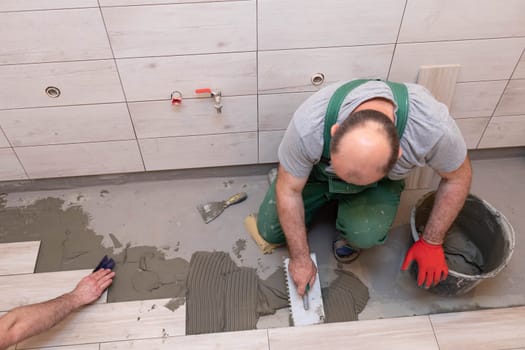 Professional construction worker laying ceramic tiles on the floor in the bathroom room.