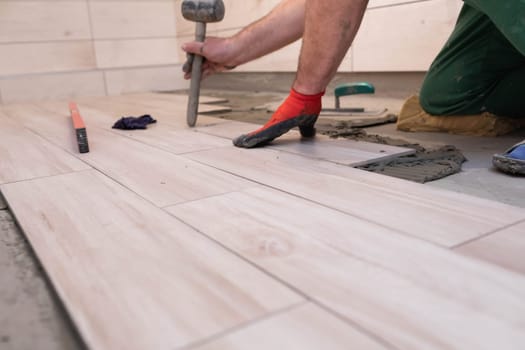 Rubber hammer. An experienced construction worker. Laying terracotta in the bathroom. Work clothes. He knocks with a hammer.