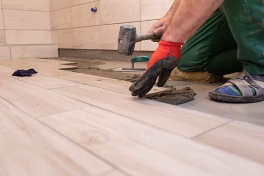Rubber hammer. An experienced construction worker. Laying terracotta in the bathroom. Work clothes. He knocks with a hammer.