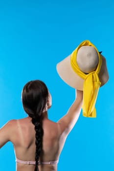 A young adult with braided hair holds a large hat high up.