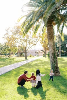 Parents with a little daughter squatted in the park in front of a small girl. High quality photo