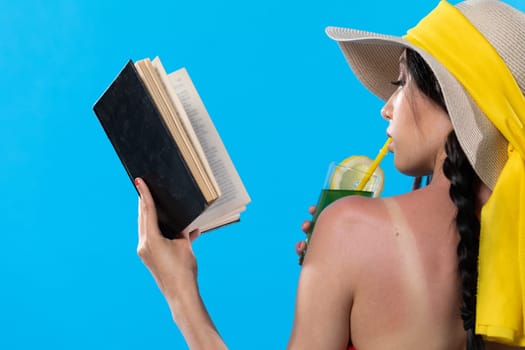 The teenager takes a sun bath and relax reading a romantic book and sipping a drink.