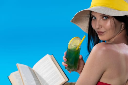 The teenager takes a sun bath and relax reading a romantic book and sipping a drink.