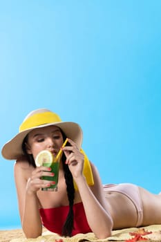 While sunbathing on the beach, a teenager drinks a cold alcoholic drink.