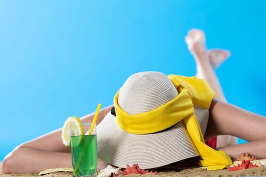 While sunbathing on the beach, a teenager drinks a cold alcoholic drink.