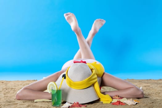 While sunbathing on the beach, a teenager drinks a cold alcoholic drink.