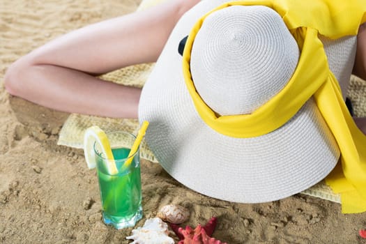 While sunbathing on the beach, a teenager drinks a cold alcoholic drink.