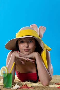 While sunbathing on the beach, a teenager drinks a cold alcoholic drink.