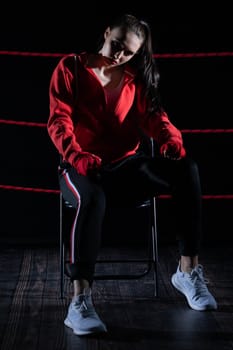 A lost fight of a strong player. He is sitting in a chair. Right after losing the fight. Sad woman after a fight in the ring. In a hoodie.