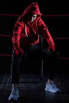 A lost fight of a strong player. He is sitting in a chair. Right after losing the fight. Sad woman after a fight in the ring. In a hoodie.