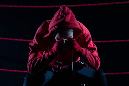 A lost fight of a strong player. He is sitting in a chair. Right after losing the fight. Sad woman after a fight in the ring. In a hoodie.
