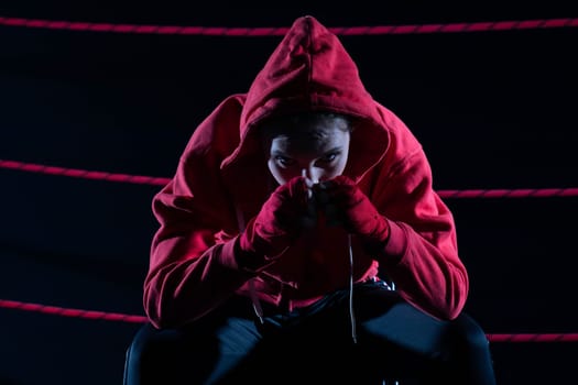 A lost fight of a strong player. He is sitting in a chair. Right after losing the fight. Sad woman after a fight in the ring. In a hoodie.