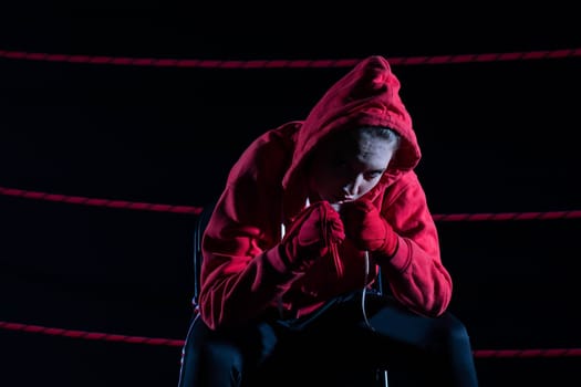 A lost fight of a strong player. He is sitting in a chair. Right after losing the fight. Sad woman after a fight in the ring. In a hoodie.
