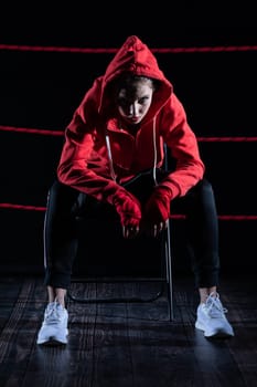 A lost fight of a strong player. He is sitting in a chair. Right after losing the fight. Sad woman after a fight in the ring. In a hoodie.