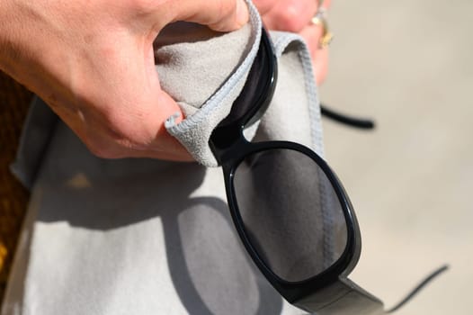 stylishly dressed young woman wipes sunglasses with microfiber, close-up view, high quality photo