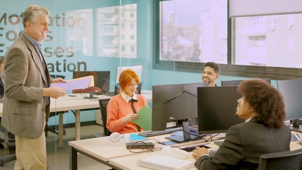 Male mature boss delivers work folders to his employees in a coworking office