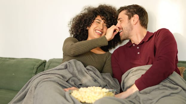 Woman putting popcorn in her boyfriend's mouth while they watch a movie at home