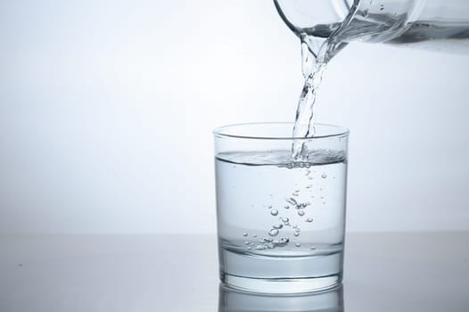 Purified water is poured from a glass jug into a glass.