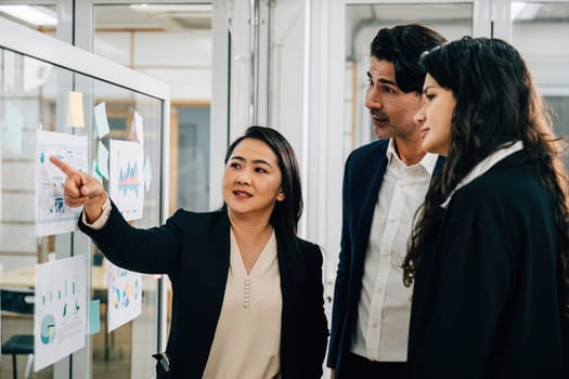 Collaborative meeting takes place around a whiteboard, with a diverse group of colleagues actively discussing ideas, strategies, and goals. Effective teamwork, brainstorming, and leadership in action.