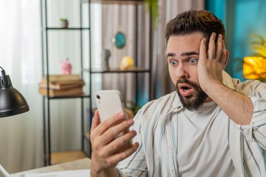 Oh my God wow. Disbelief. Happy amazed shocked young businessman working on smartphone shocked by sudden victory game winning lottery app goal achievement good news. Man freelancer guy at home office.