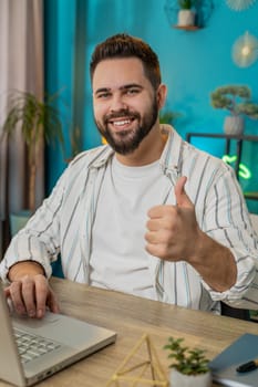 Like. Smiling young Caucasian business man looking approvingly at camera showing double thumbs up sign positive something good great news positive feedback. Happy guy at home office desk. Vertical