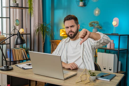 Dislike. Upset Caucasian business man at home office room showing thumbs down sign gesture, expressing discontent, disapproval dissatisfied bad work feedback. Displeased guy freelancer. Lifestyle
