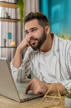Caucasian man entrepreneur prepares startup project for presentation finds idea. Employee freelancer think typing browsing using laptop computer at home office desk. Remote distant working. Vertical