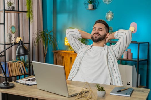 Happy Caucasian man after finishing working on laptop pc. Guy freelancer working online, remote job at home office table workplace. E-learning, browsing internet on notebook computer. Lifestyle