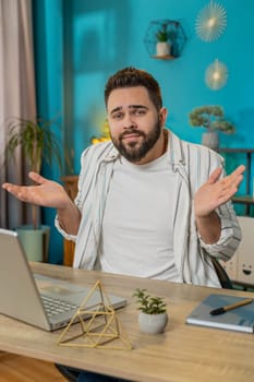 I don't know what to say. Confused young Caucasian man feeling embarrassed about ambiguous question, having doubts, no idea, being clueless and uncertain. Guy at home office table workplace. Vertical