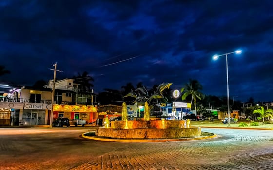 Busy road street driving cars vehicles traffic jam and traffic circle roundabout with dolphin dolphins sculpture statue with fountain at night in Zicatela Puerto Escondido Oaxaca Mexico.